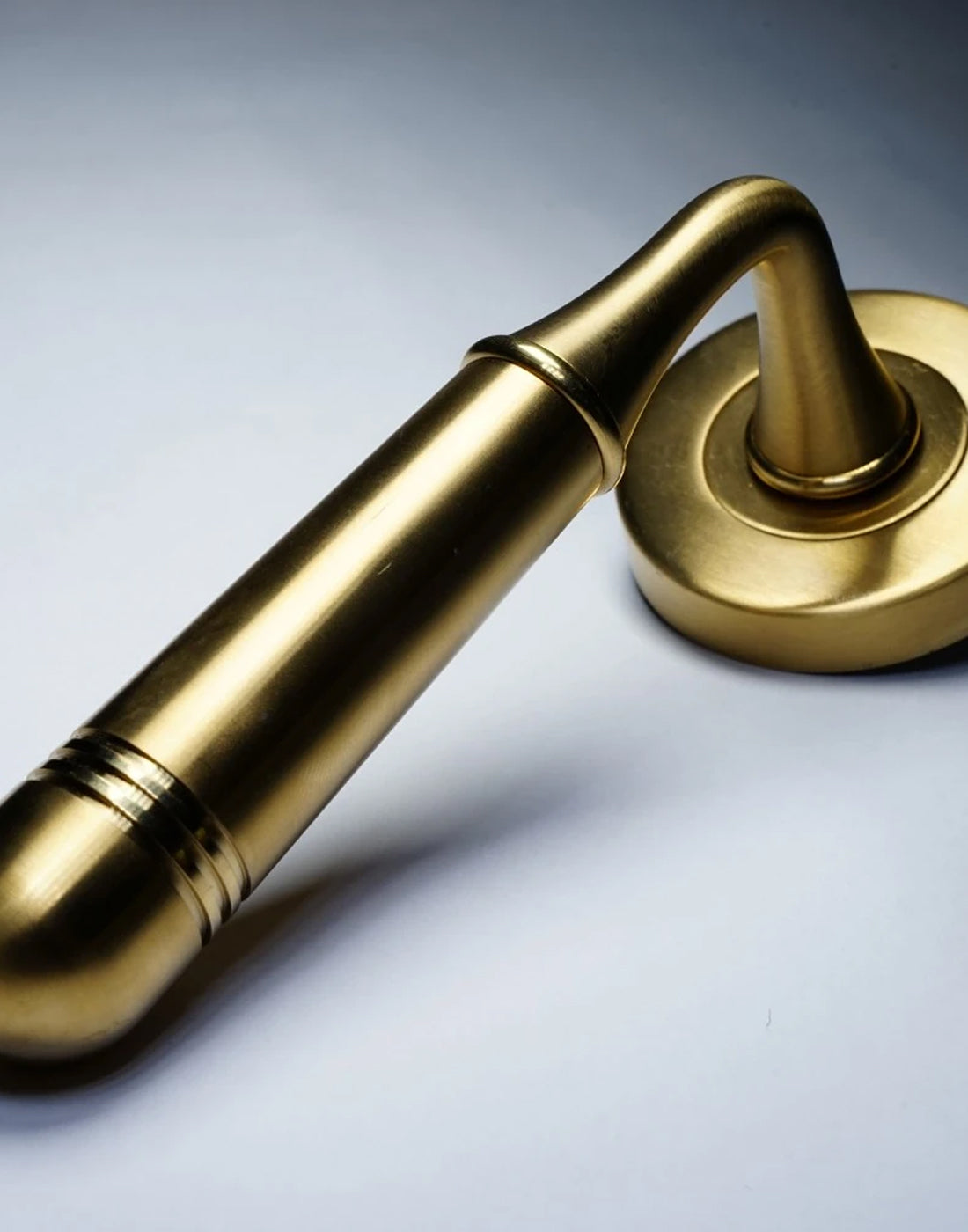Satin brass Opera lever door handle on round rose on a light grey background