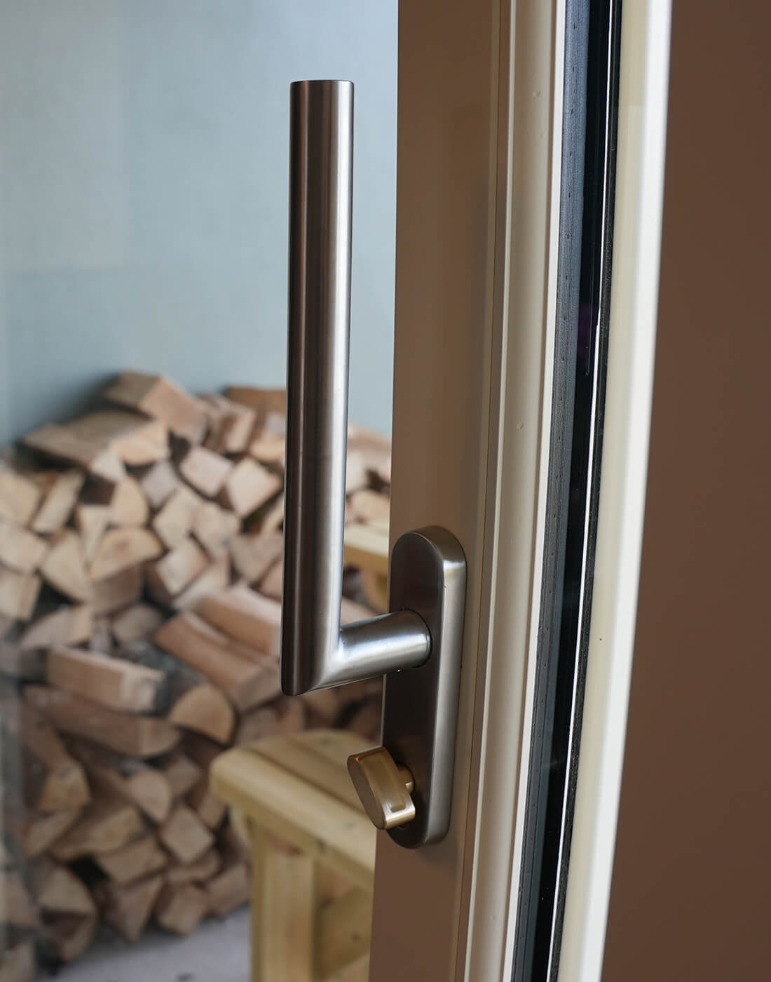 Close-up of a lift and slide BLU door handle and thumb turn from Coastal on a glass door with stacked firewood in the background.