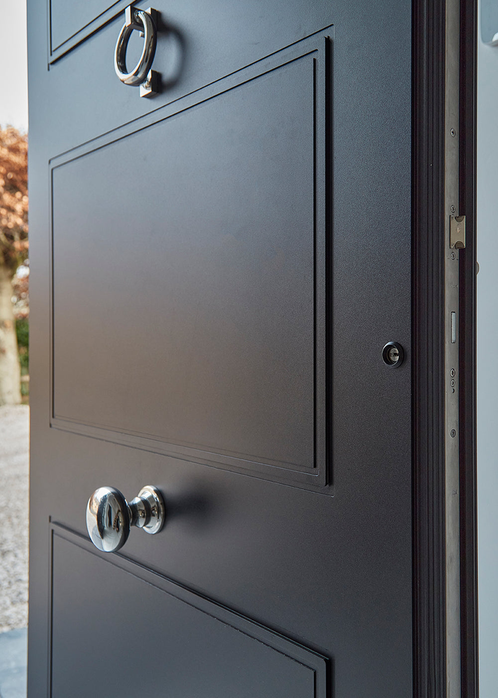 Close-up of a dark grey door with a polished stainless steel doorknob and ring door knocker from Coastal Group.