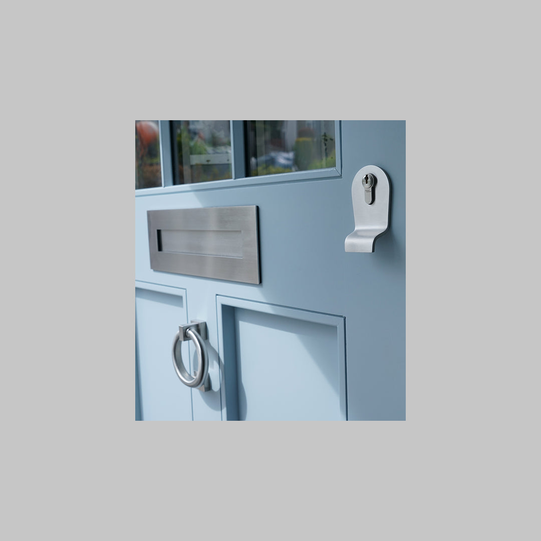 Light blue door with satin stainless steel letter box, cylinder pull and ring door knocker on a grey background