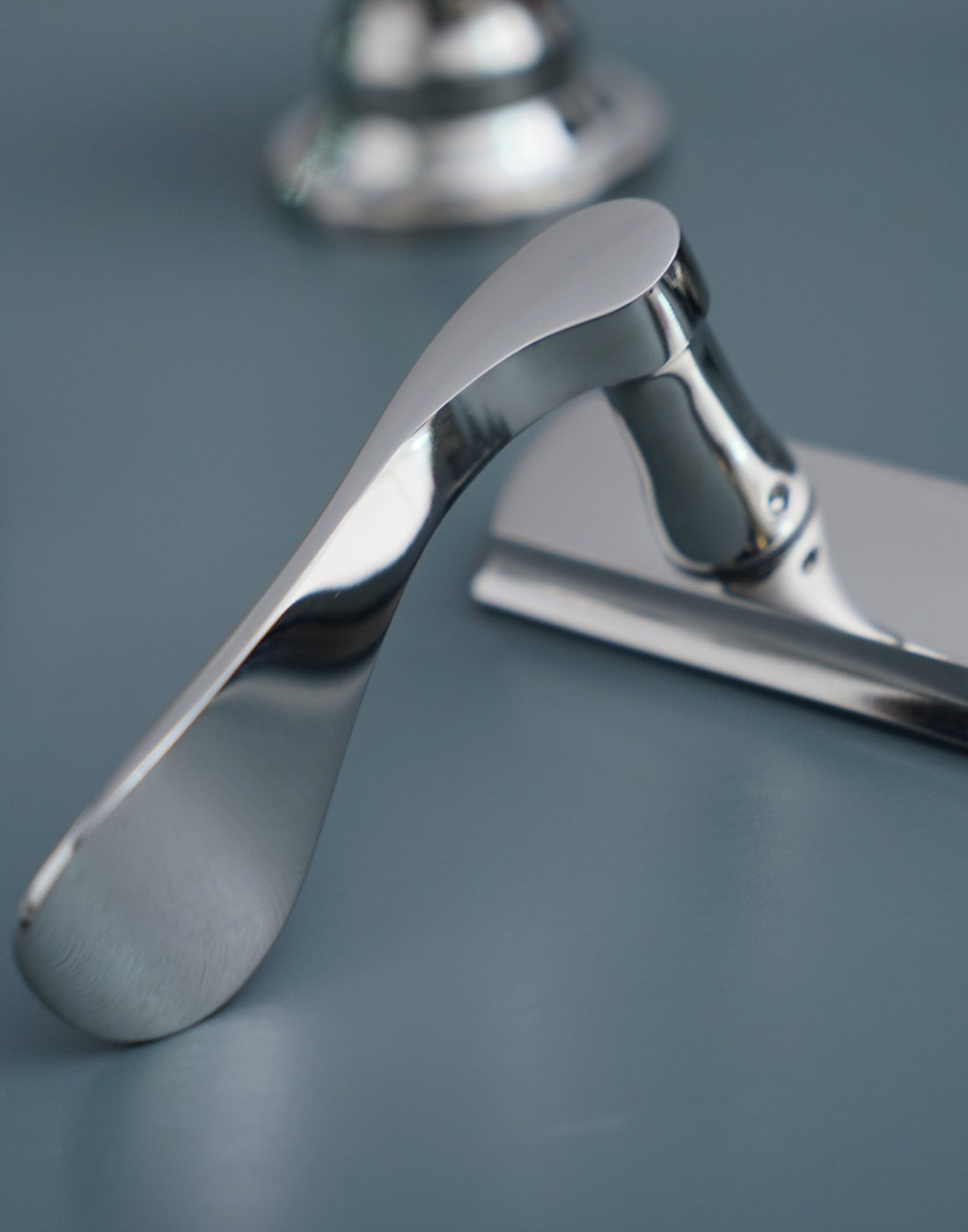 Polished stainless steel Regent lever door handle on backplate from Coastal on a light blue background