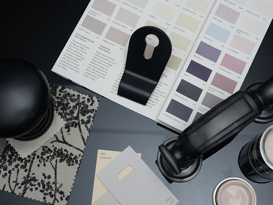 Black door handles, doctor's door knocker and door knob item on a surface with colour swatches and samples in the background